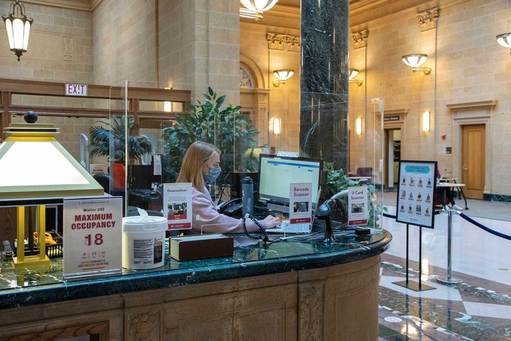 Worker at Great Hall service desk with plexiglass and max occupancy sign
