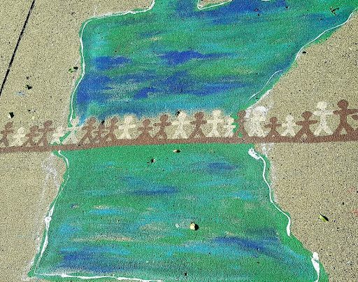 Sidewalk chalk drawing of state of Minnesota with a line of brown and white stick figure people across the state.