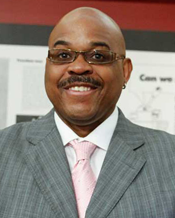 Headshot of smiling man wearing a gray blazer with a pink tie