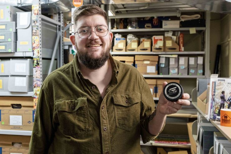 Aiden Bettine hold a hockey puck from the Twin Cities Gay Hockey Association, which is held in the UMN Tretter Collection. (Photo/Adria Carpenter)