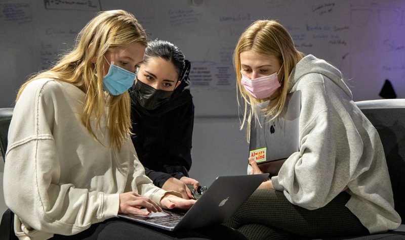 Three female presenting students working together.