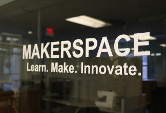 Image of the Makerspace sign that is on the window next to the Makerspace entrance. White text states "Makerspace" on top with "Learn. Make. Innovate." underneath. Background is dark because lights are off in the Makerspace.