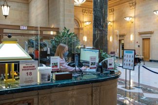 Worker at Great Hall service desk with plexiglass and max occupancy sign