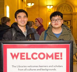 Welcome to the Libraries. Two students stand behind a Welcome sign in Walter Library. 