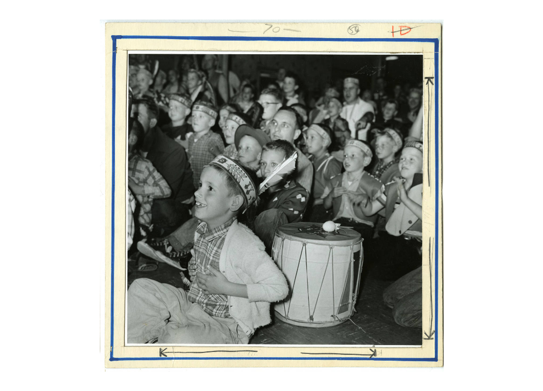 Boys with Indian Guides headbands and feathers seated on the floor with a drum, sometime between 1950 and 1970.