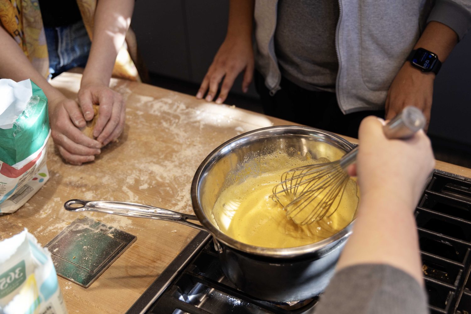 A student whisks their sabayon sauce, which is heating in a metal mixing bowl placed directly above a small saucepan full of boiling water