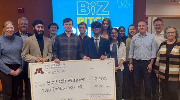 A group of students and judges in front of a monitor that reads Biz Pitch. Students in the front row hold a large check that reads BizPitch Winner $2,000.00.