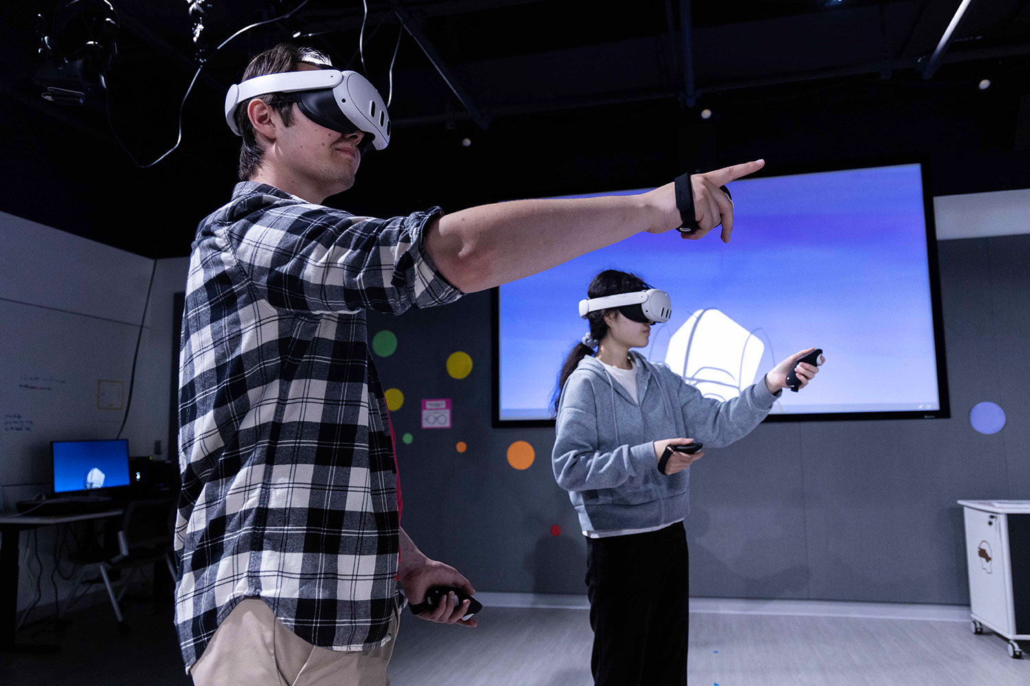 Two students in virtual reality headsets pointing to a screen in the VR studio in the Health Sciences Library